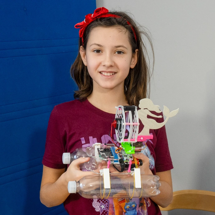 Student holding a BottleBoat made from plastic bottles with a micro:bit controller and a mermaid-shaped rudder.